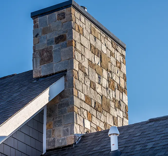 Large Stone Cladding covered masonry chimney on top of a asphalt roof