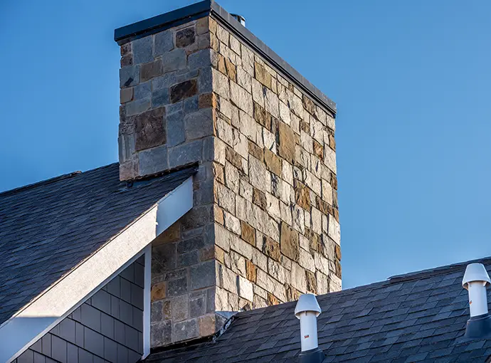 Large Stone Cladding covered masonry chimney on top of a asphalt roof